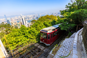 Die beliebte rote Peak Tram zum Victoria Peak, dem höchsten Gipfel der Insel Hongkong. Touristische Straßenbahn mit Panoramablick auf die Skyline der Stadt im Hintergrund an einem sonnigen Tag.