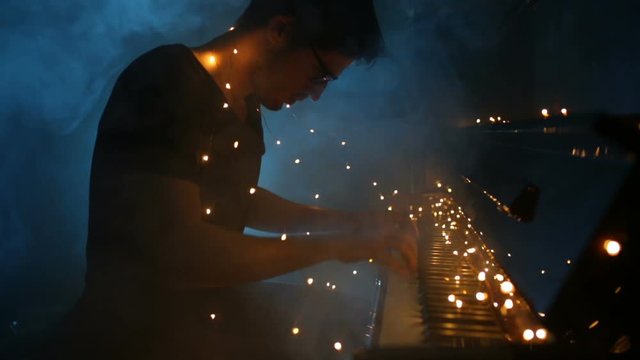 Boy is playing piano with some Christmas Light on the keys. Smoke on the background.
