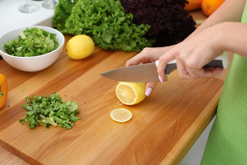 Closeup of woman hands cooking vegetables salad in kitchen. Housewife cuts lemon. Healthy meal and vegetarian concept.