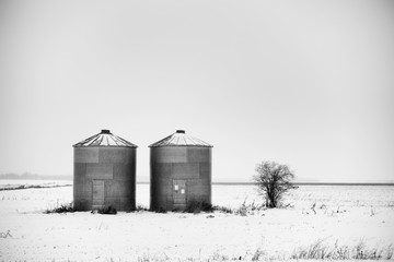 Two flat bottom steel grain bins in a rural black and white winter landscape © kat7213