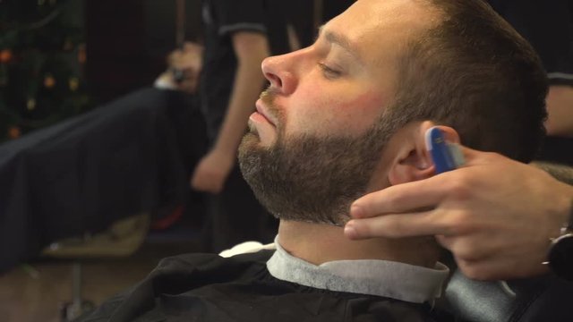 Barberman shaving beard of man