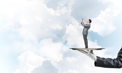 Businessman on metal tray playing fife against blue sky background