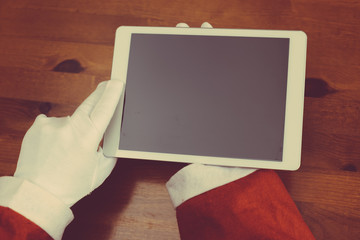 Santa Claus working using digital tablet computer screen on wooden table background. Close up top view on hands