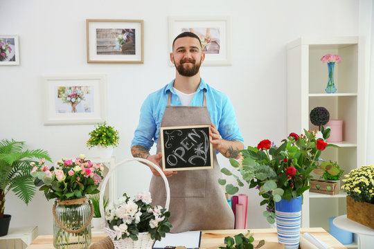 Handsome bearded florist holding board with inscription OPEN