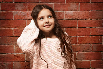 Cute little girl in warm sweater standing near brick wall