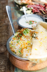 Authentic chicken biryani served with naan bread, fragrant pilau rice and yoghurt, in a metal pot...