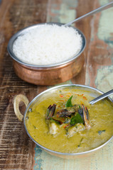 A delicious spicy prawn green curry, served with sticky rice in a rustic metal pan.