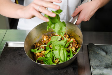 Mixing a curried cauliflower, spinach and potato sauce, in a metal pan.