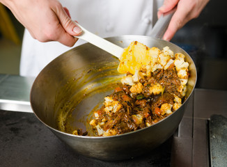 Mixing a curried cauliflower, spinach and potato sauce, in a metal pan.