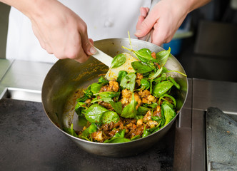 Mixing a curried cauliflower, spinach and potato sauce, in a metal pan.