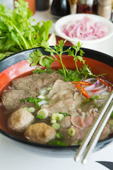 A bowl of traditional vietnamese beef and chicken pho street food, surrounded by fresh herbs. Pho is a vietnamese noodle soup consisting of meat, herbs, chilli, coriander and dumplings.