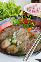A bowl of traditional vietnamese beef and chicken pho street food, surrounded by fresh herbs. Pho is a vietnamese noodle soup consisting of meat, herbs, chilli, coriander and dumplings.