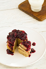 Pancakes stack with banana, coconut flour and blueberry jam on a white plate.  Bright healthy breakfast. White wooden table