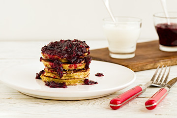 Pancakes stack with banana, coconut flour and blueberry jam on a white plate.  Bright healthy breakfast. White wooden table