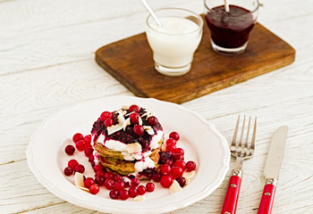 Stack of vegan gluten free pancakes with yogurt, blueberrty jam and canberries on a white plate with red fork and knife. Bright healthy breakfast. White wooden table