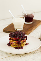 Pancakes stack with banana, coconut flour and blueberry jam on a white plate.  Bright healthy breakfast. White wooden table