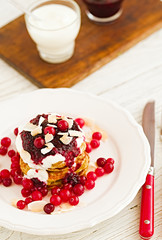 Stack of vegan gluten free pancakes with yogurt, blueberrty jam and canberries on a white plate with red fork and knife. Bright healthy breakfast. White wooden table