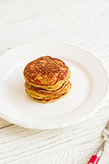 Plain paleo pancakes with banana and coconut on a white plate with red fork and knife. Bright healthy breakfast. White wooden table