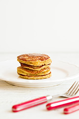 Plain paleo pancakes with banana and coconut on a white plate with red fork and knife. Bright healthy breakfast. White wooden table