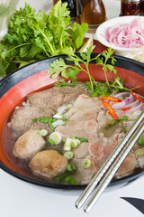 A bowl of traditional vietnamese beef and chicken pho street food, surrounded by fresh herbs. Pho is a vietnamese noodle soup consisting of meat, herbs, chilli, coriander and dumplings.