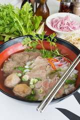 A bowl of traditional vietnamese beef and chicken pho street food, surrounded by fresh herbs. Pho is a vietnamese noodle soup consisting of meat, herbs, chilli, coriander and dumplings.