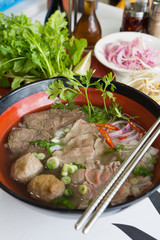 A bowl of traditional vietnamese beef and chicken pho street food, surrounded by fresh herbs. Pho is a vietnamese noodle soup consisting of meat, herbs, chilli, coriander and dumplings.