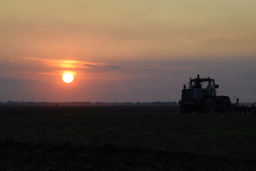 Fototapeta premium Tractor plowing plow the field on a background sunset. tractor silhouette on sunset background