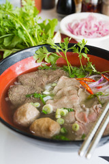 A bowl of traditional vietnamese beef and chicken pho street food, surrounded by fresh herbs. Pho is a vietnamese noodle soup consisting of meat, herbs, chilli, coriander and dumplings.