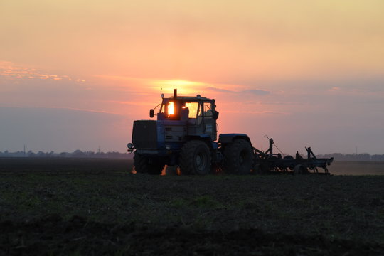 Tractor plowing plow the field on a background sunset. tractor silhouette on sunset background