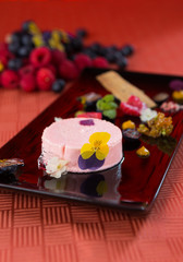A beautiful rich gourmet blueberry and raspberry cheesecake, garnished with rose petals on a modes black plate.