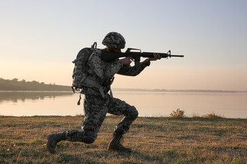 Silhouette of soldier with rifle near river at sunset
