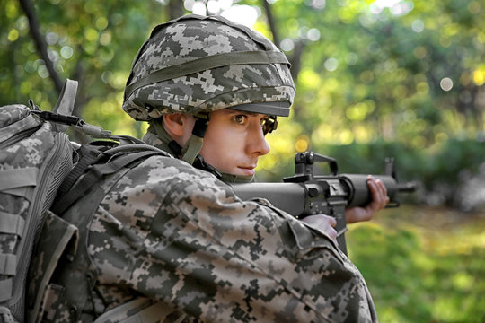 Soldier taking aim from rifle in forest, close up view