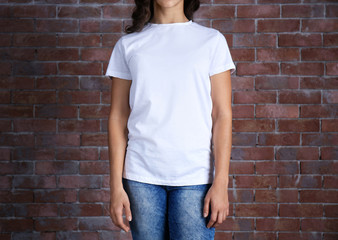 Young woman in blank white t-shirt standing against brick wall, close up
