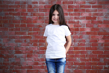 Little girl in blank white t-shirt standing against brick wall