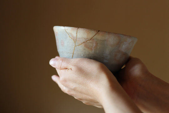 金継ぎされたピンクの萩焼の抹茶茶碗を両手で持つ女性｜ぼかした背景