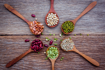 Close up  of various beans in wooden spoons setup on shabby wooden background.