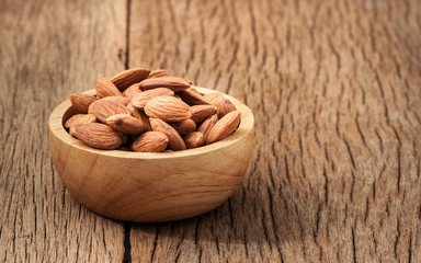 Closeup almonds kernels in wooden bowl with   on rustic wooden b