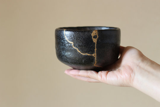 金継ぎの黒い楽茶碗を女性が右手で持つ（ぼかし背景）