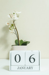 Closeup white wooden calendar with black 6 january word with white orchid flower on white wood desk and cream color wallpaper in room textured background , selective focus at the calendar