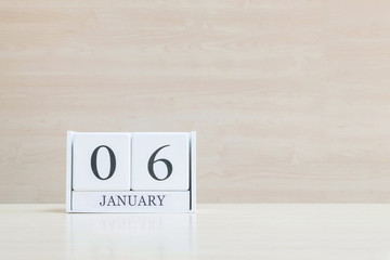 Closeup surface white wooden calendar with black 6 january word on blurred brown wood desk and wood wall textured background with copy space , selective focus at the calendar