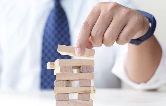Businessman gambling placing wooden block on a tower. Planning, risk and strategy in business