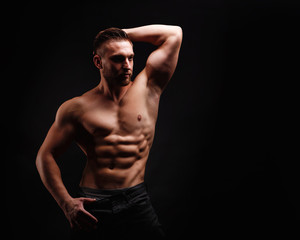Fototapeta na wymiar Bodybuilder posing on a black background. Dramatic portrait of an athlete. Drying. Relief and sculptural muscles of the body. Healthy lifestyles concept. Abdominal muscles and triceps.