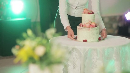 Waiter brings wedding cake and puts it on table under photo flash lights close up no face. Beautiful wedding cake decoration with natural roses blooms and berries. Banquet arrangement and catering