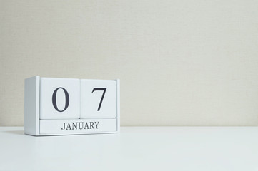 Closeup white wooden calendar with black 7 january word on blurred white wood desk and cream color wallpaper in room textured background with copy space , selective focus at the calendar