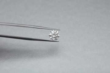 loose big brilliant diamond being held by a tweezers on a grey silver background