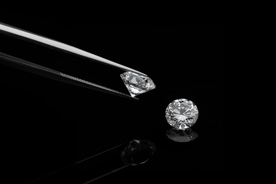 loose brilliant diamonds, one is being held by a tweezers on reflective black background