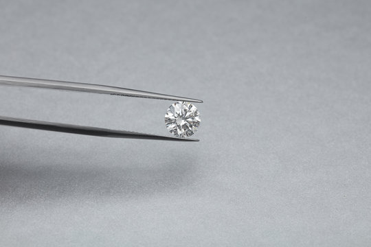 loose big brilliant diamond being held by a tweezers on a grey silver background