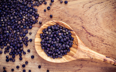 Closeup black pepper in wooden spoon on shabby teak wood table.