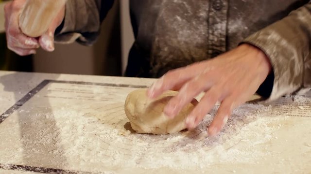 woman baker presses dough ball onto counter - close up