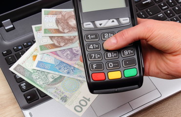 Hand of woman using payment terminal, polish currency money on laptop